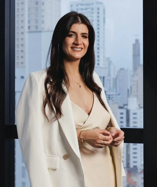 Daglia Santis, de blazer creme, diante da janela com as torres de Balneário Camboriú